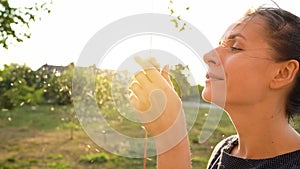 Woman blows on reeds outdoors in sunny day. Fluff from reeds flies around. Slow motion