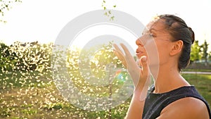 Woman blows on reeds outdoors in sunny day. Fluff from reeds flies around. Slow motion