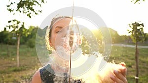 Woman blows on reeds outdoors in sunny day. Fluff from reeds flies around. Slow motion