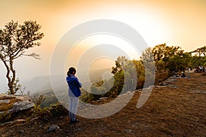 Woman in blue coat looking sunset at cliff in winter