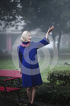 Woman in a blue coat near a park bench.