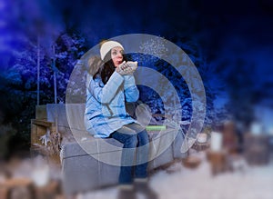 Woman in blue down jacket blows snowflakes while sitting on a sw