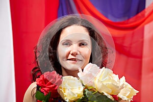 Woman in blue dress with long brunette curly hair and roses in hands indoors with red and blue background. Model posing