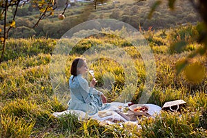 A woman in blue dress sits on a picnic in a park with panoramic view