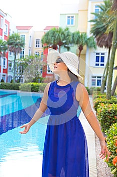 Woman in blue dress and white hat smiling by the swimming pool
