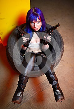 Woman with blue haircut in leather wear holding two guns sirs in the tire