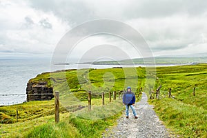 Woman in blue jacket pausing on the coastal route walk from Doolin to Cliffs of Moher