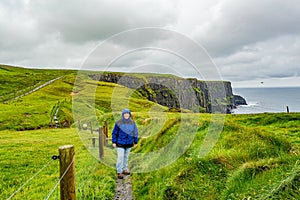 Woman in blue jacket walking the coastal walk route from Doolin to the Cliffs of Moher