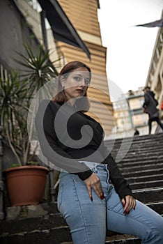 Woman in blue jeans and black blouse posing on stairs