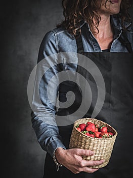 Woman in blue jeans shirt holding the basket full of strawberry