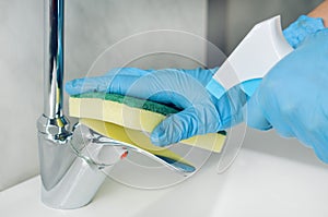 Woman with blue nitrile gloves disinfects the sink mixer after washing her hands to avoid the proliferation of viruses and photo