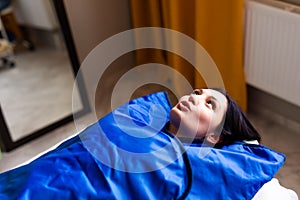 Woman in blue pressotherapy suit lying down having pressure therapy for weight loss in spa salon. Doctor help lose weight and