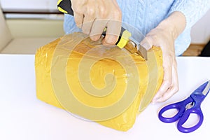 A woman in blue pullover unpacks, unbox an orange parcel with scissors and a knife