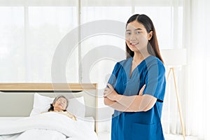 A woman in a blue scrubs stands in front of a bed with a woman lying on it