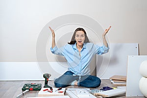 Woman in blue shirt sitting on the floor with tools to assemble furniture