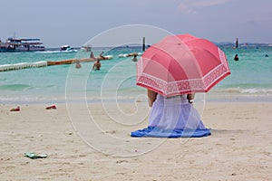 Woman in blue suit with red umbrella sat on the beach