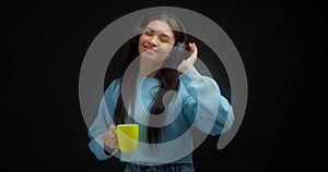 Woman in a blue sweater enjoys music with headphones, drinks from a yellow mug