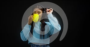 Woman in a blue sweater enjoys music with headphones, drinks from a yellow mug