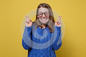 Woman in blue sweater and glasses smiling crossing fingers with hope