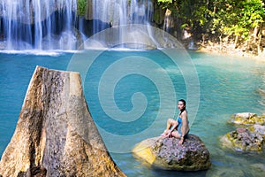 Woman in blue swimsuit sit enjoy at Erawan Waterfall and natural