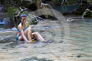 Woman in blue swimsuit sit happy at  Erawan Waterfall