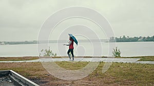 woman with blue umbrella walks along the coast on cloudy day