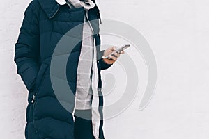 Woman in blue winter jacket and sweater with phone in hand