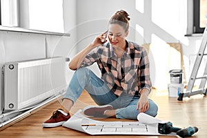 woman with blueprint calling on smartphone at home