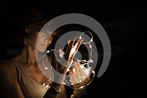 Woman, blurred face, holding string lights in the dark. Copy space