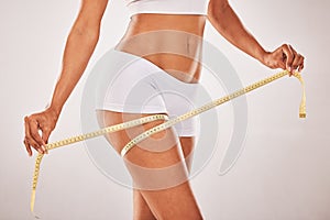 Woman, body and lose weight with tape measure on thigh for healthy diet, health and wellness. Model studio background