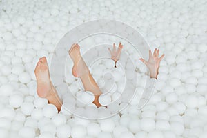 Woman body parts stick out white plastic balls in the dry pool. Copy splace.