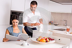 Woman with book while man pouring tea