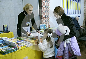 Woman bookseller selling little girl and her mother book, bookstore. Book Fair. Kyiv, Ukraine