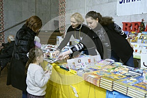 Woman bookseller selling little girl and her mother book, bookstore. Book Fair. Kyiv, Ukraine