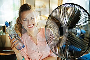 Woman with bottle of water enjoying fresh air in front of fan