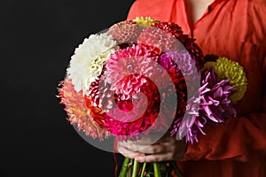 Woman with bouquet of beautiful dahlia flowers on black background, closeup