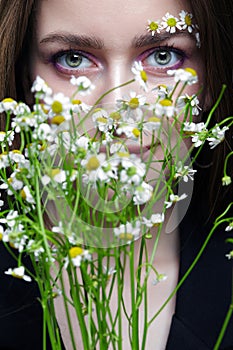 Woman with bouquet of daisies and brows decorated by small chamomile flowers