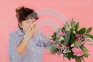 Woman bouquet of flowers hands take hankie sneezes closed eyes concept allergy illness discomfort pink background