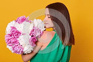 Woman with bouquet of pink and white peonies in hands, posing backwards, girl in light transparent dress. Dark haired lady holding