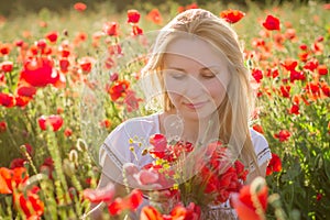 Woman with bouquet among poppies field at sunset