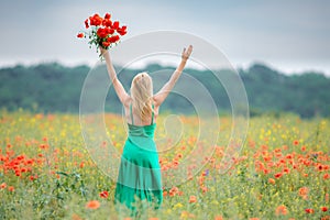 Woman with bouquet of poppies and raised hands sky among the flo