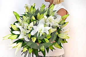 Woman with bouquet of white lilies. Beautiful fresh delicate flowers for holiday. Woman with beautiful flowers in her hands