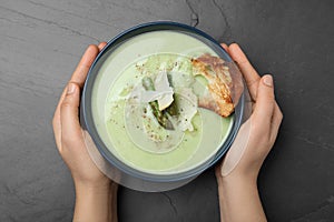 Woman with bowl of delicious asparagus soup at dark table, top view