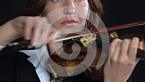 Woman bows over the strings of a violin. Black background. Close up