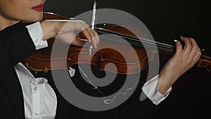 Woman bows over the strings of a violin . Black background. Close up