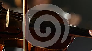 Woman bows over the strings of a violin . Black smoke background. Close up