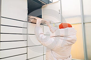 Woman with box at outdoor automated parcel machine. Modern parcel locker with many postal boxes outdoors