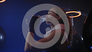 Woman boxer is drinking water after the training, feeling thirsty and carrying the white towel on her shoulders