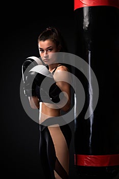 Woman boxer fighting in gloves with boxing punching bag on black background. Boxing and fitness concept.