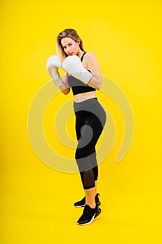 Woman boxer in gloves training on yellow and dark studio background